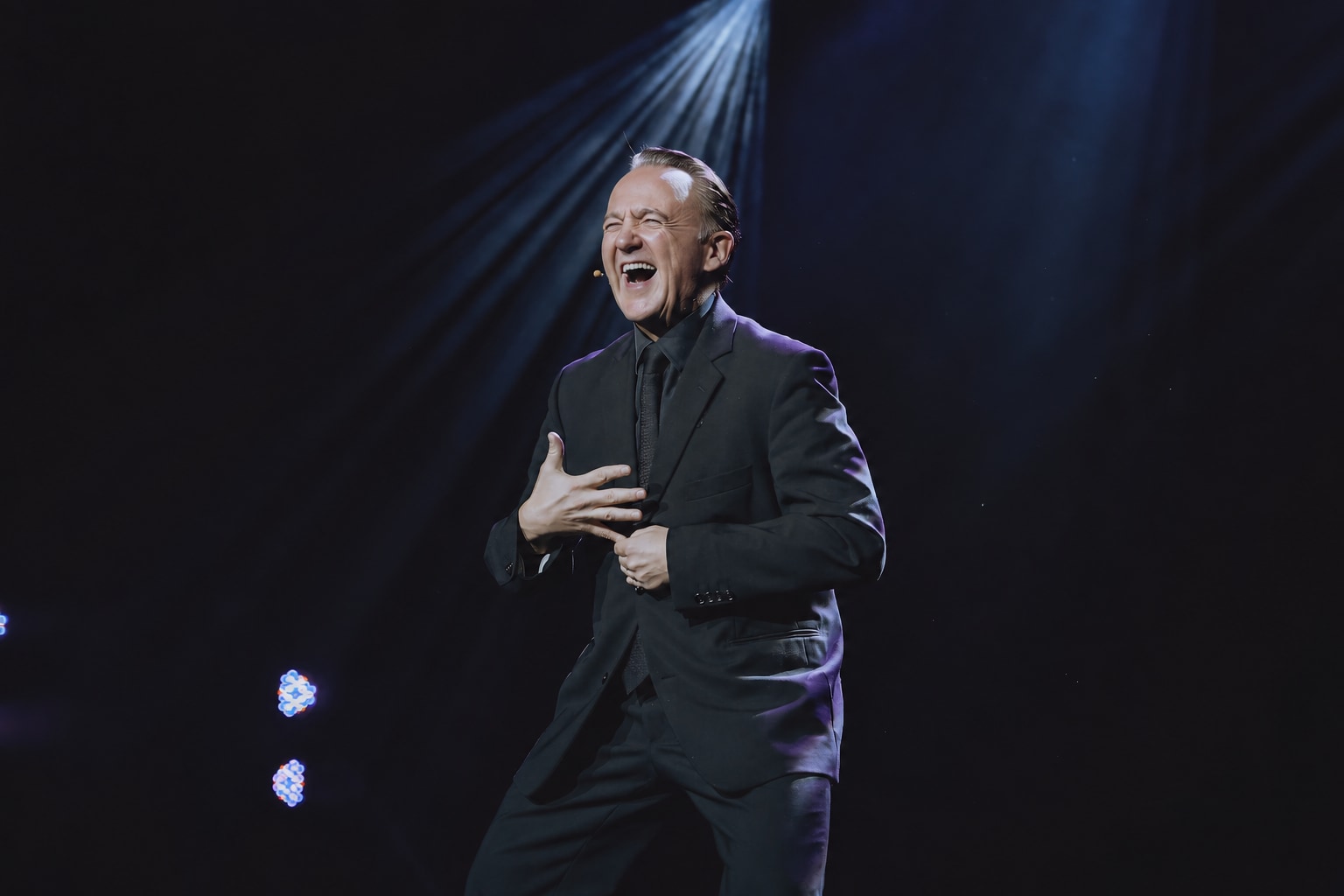 Norbert Ferré laughing on stage, with one hand over his heart.