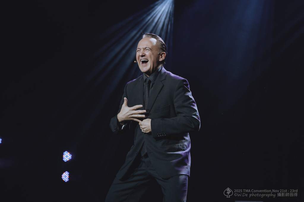Norbert Ferré laughing on stage, with one hand over his heart.