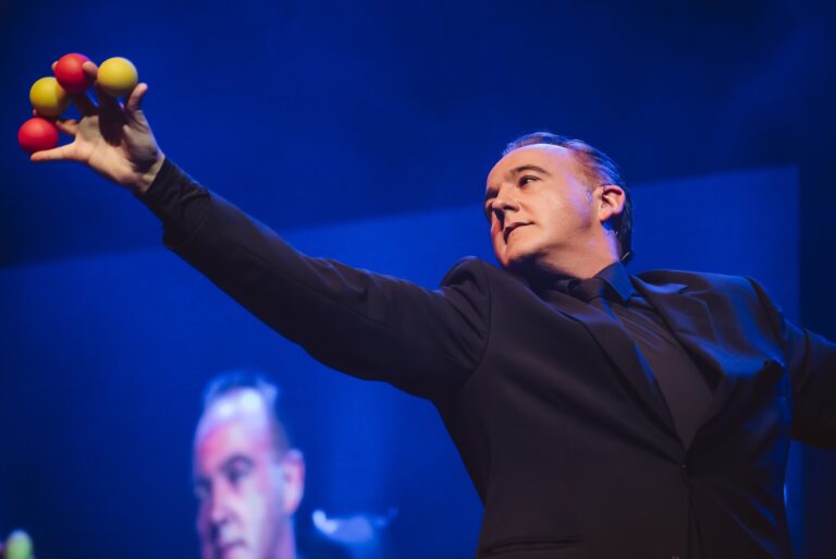 Norbert Ferré holding coloured balls in his raised hand on stage.