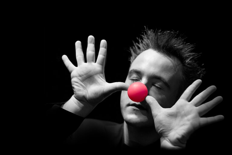 Norbert Ferré, les yeux fermés et les mains ouvertes autour d’une balle rouge sur le nez